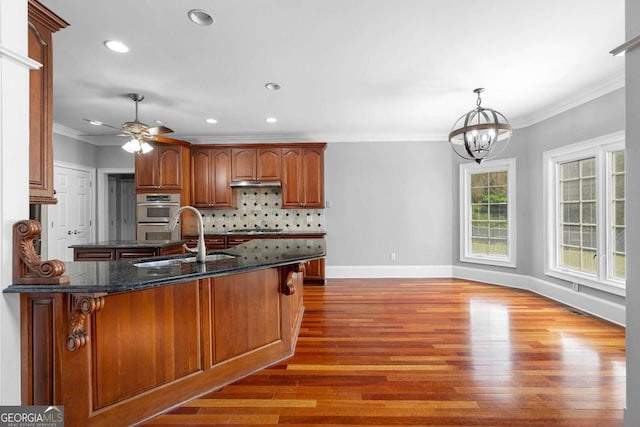 kitchen with a sink, ornamental molding, appliances with stainless steel finishes, under cabinet range hood, and backsplash