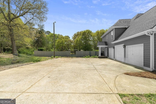 view of patio featuring concrete driveway, fence, and a garage