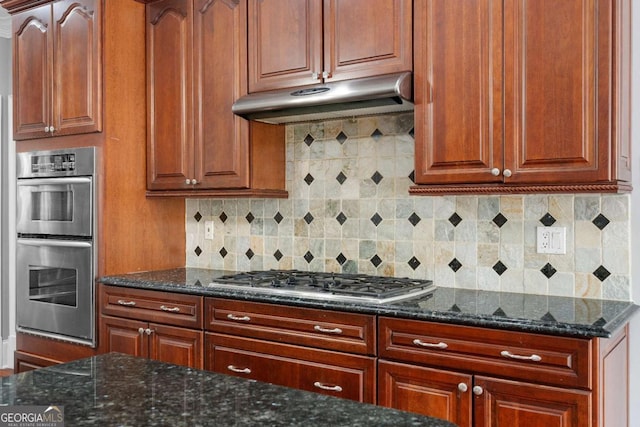 kitchen with dark stone countertops, tasteful backsplash, stainless steel appliances, and under cabinet range hood