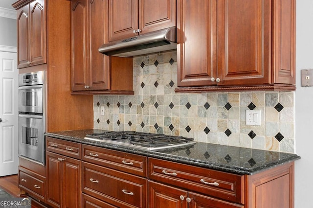 kitchen with dark stone countertops, under cabinet range hood, backsplash, and appliances with stainless steel finishes