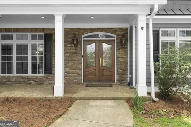entrance to property with a porch, french doors, and brick siding
