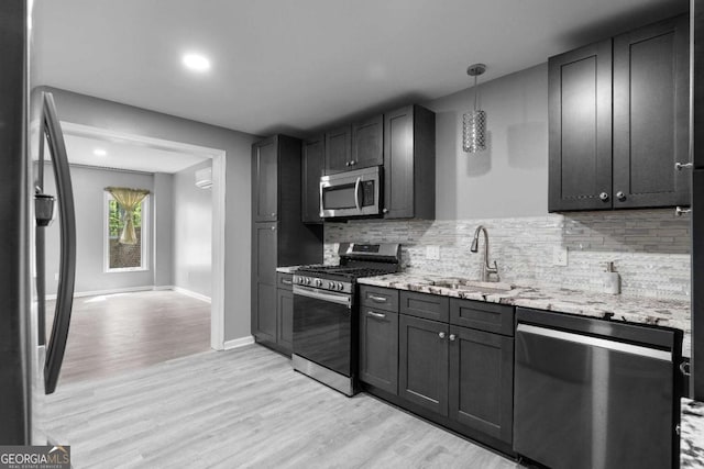 kitchen with tasteful backsplash, light stone counters, a sink, stainless steel appliances, and light wood finished floors
