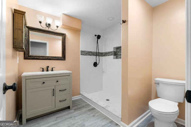 bathroom with vanity, baseboards, toilet, tiled shower, and wood finished floors