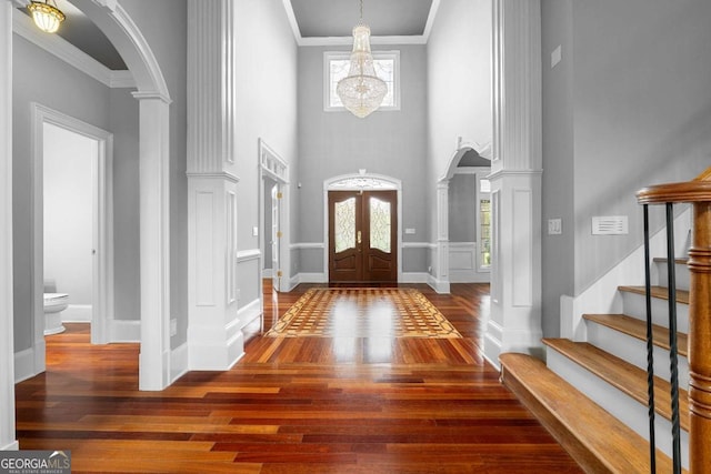 entryway with arched walkways, ornamental molding, a chandelier, wood finished floors, and french doors