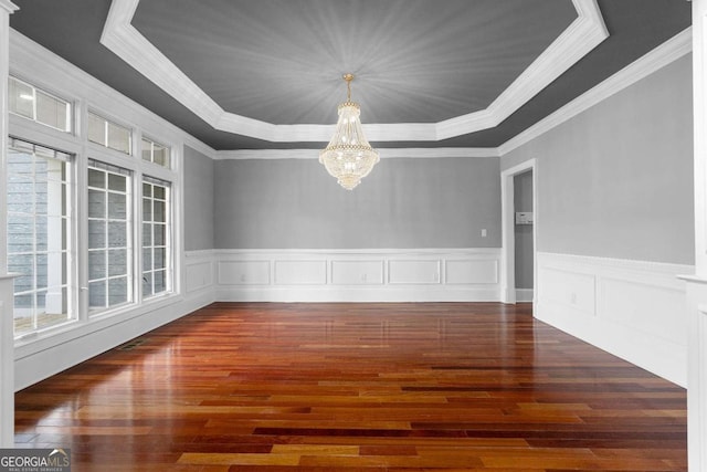 spare room featuring a raised ceiling, wood finished floors, an inviting chandelier, and a wainscoted wall