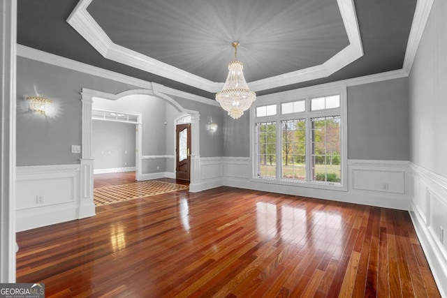 unfurnished dining area featuring a chandelier, ornate columns, a raised ceiling, arched walkways, and hardwood / wood-style flooring