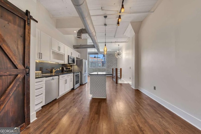 kitchen with dark wood-style flooring, white cabinetry, dark countertops, a barn door, and stainless steel appliances