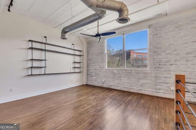 interior space with baseboards, brick wall, visible vents, ceiling fan, and wood finished floors
