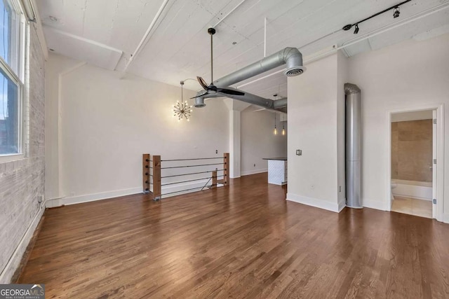 unfurnished living room with brick wall, rail lighting, wood finished floors, and baseboards