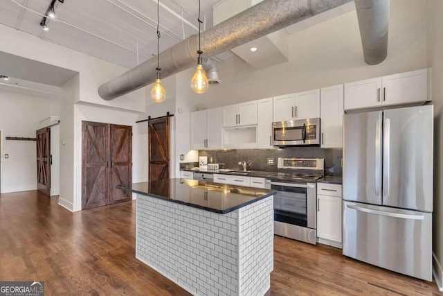 kitchen with a towering ceiling, a barn door, appliances with stainless steel finishes, dark countertops, and decorative backsplash