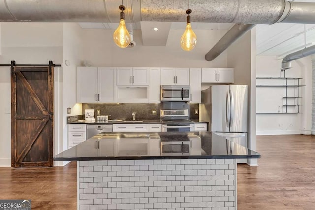 kitchen with dark wood finished floors, white cabinets, dark countertops, stainless steel appliances, and backsplash