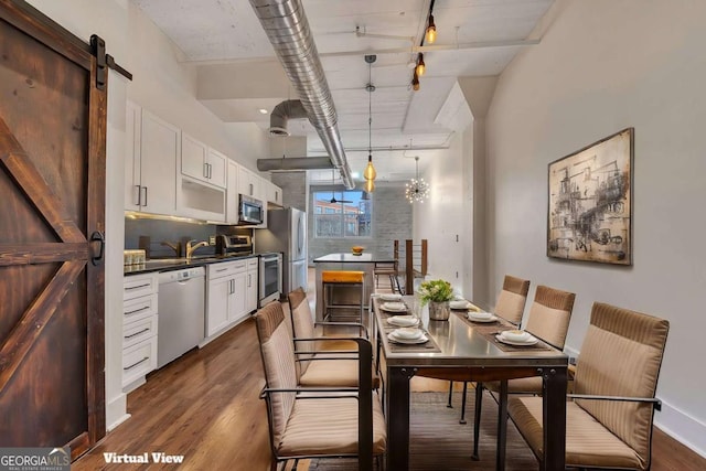 dining space with dark wood-style flooring, baseboards, rail lighting, and a barn door