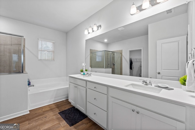 full bathroom featuring a bath, a sink, a shower stall, double vanity, and wood finished floors