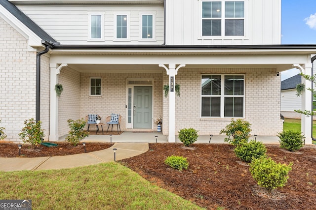 view of exterior entry with board and batten siding, covered porch, and brick siding