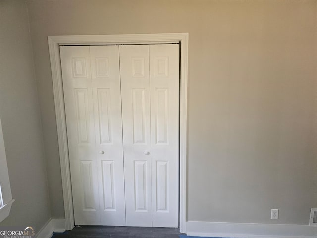 unfurnished bedroom with baseboards, a closet, dark wood finished floors, and visible vents