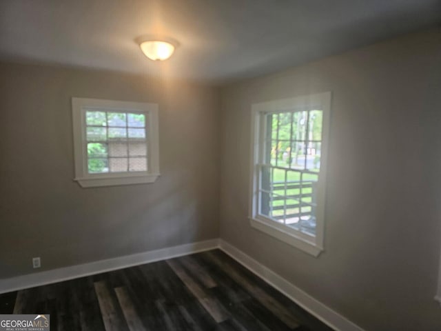 spare room featuring baseboards, dark wood finished floors, and a wealth of natural light
