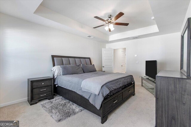 bedroom with a tray ceiling, light colored carpet, baseboards, and visible vents