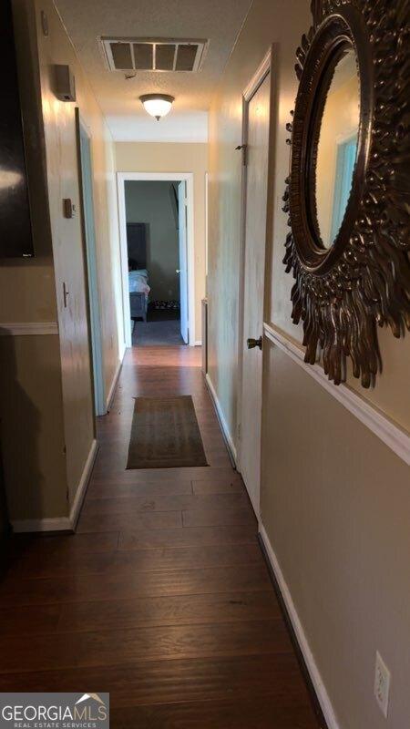 hall with visible vents, baseboards, and wood finished floors