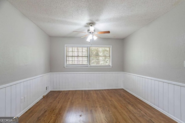 spare room featuring a textured ceiling, a ceiling fan, a wainscoted wall, wood finished floors, and a textured wall