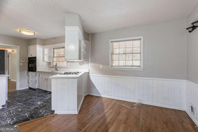 kitchen featuring white cabinets, oven, a sink, light countertops, and wainscoting