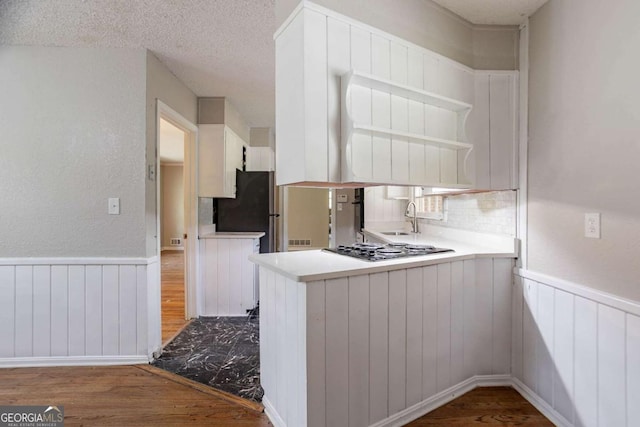 kitchen featuring open shelves, a peninsula, stainless steel gas stovetop, wainscoting, and wood finished floors