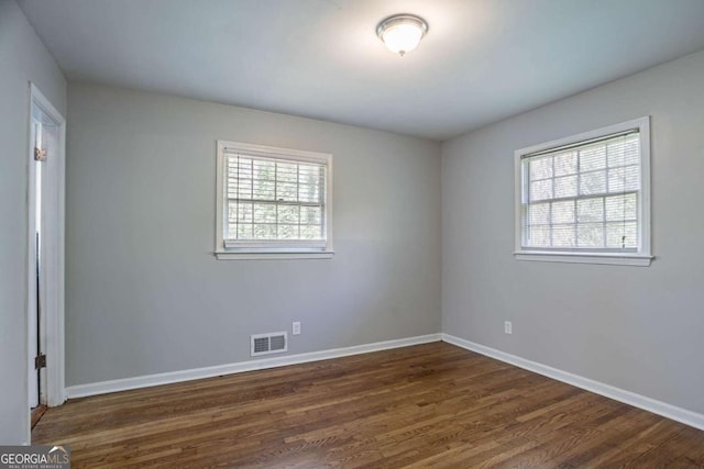 unfurnished room with visible vents, dark wood-style flooring, and baseboards