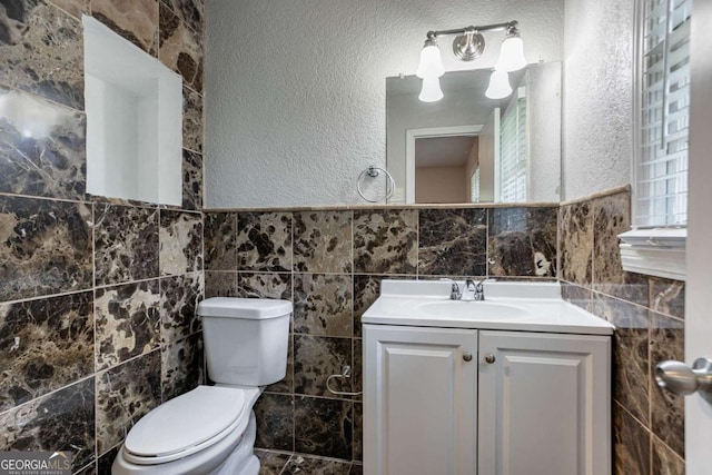 half bathroom featuring toilet, tile walls, vanity, and a textured wall