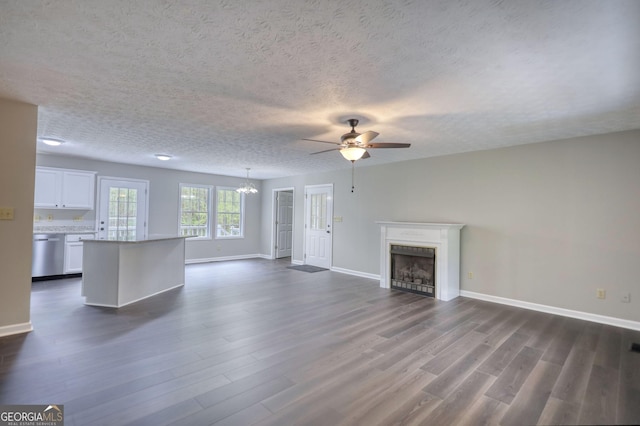 unfurnished living room featuring baseboards, dark wood-style flooring, a textured ceiling, a fireplace, and ceiling fan with notable chandelier