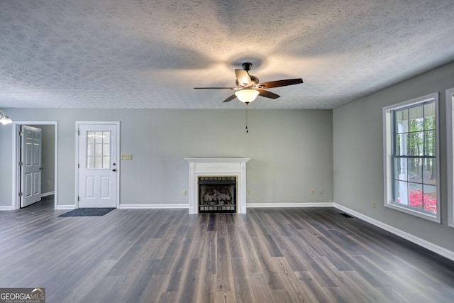 unfurnished living room featuring baseboards, a ceiling fan, a textured ceiling, a fireplace, and dark wood-type flooring