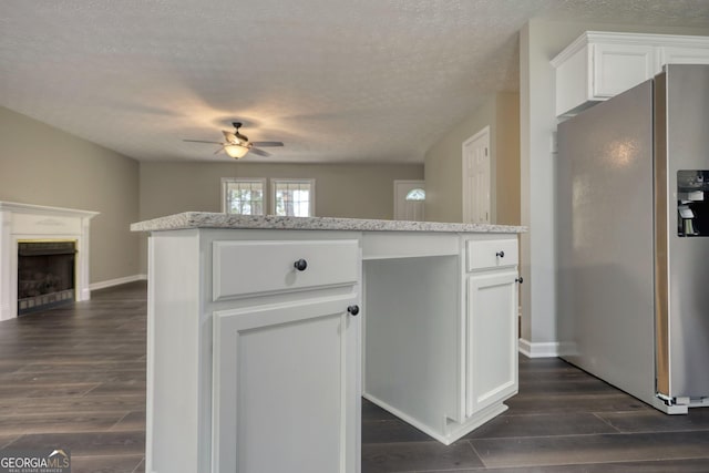 kitchen featuring stainless steel fridge with ice dispenser, a ceiling fan, a fireplace, dark wood-style floors, and white cabinetry