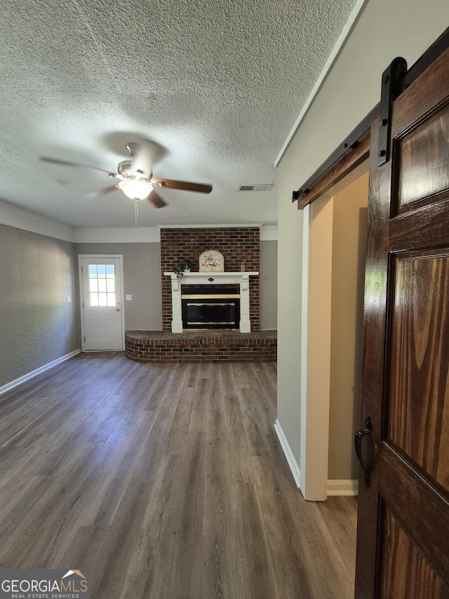 unfurnished living room with a textured ceiling, a ceiling fan, a barn door, wood finished floors, and baseboards