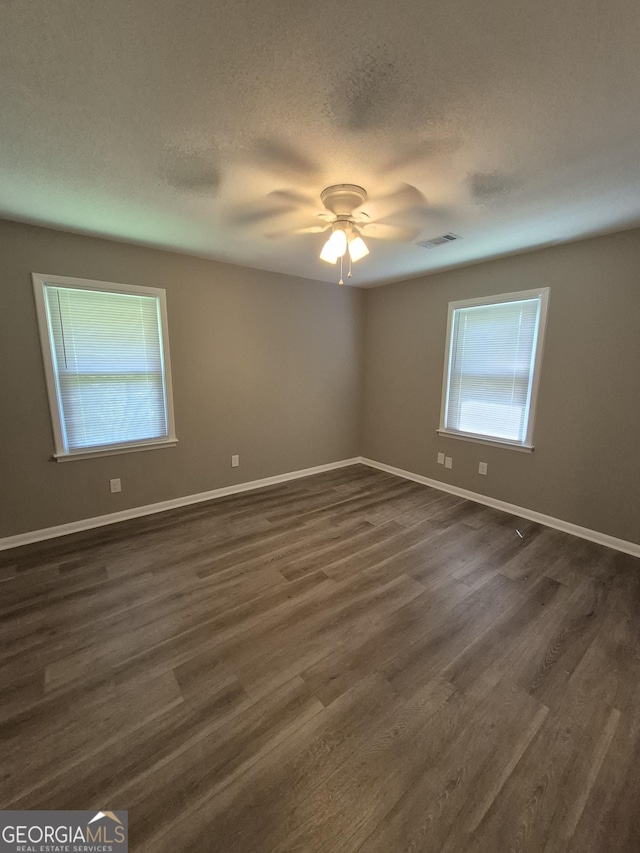 empty room with dark wood-type flooring, a textured ceiling, a ceiling fan, visible vents, and baseboards