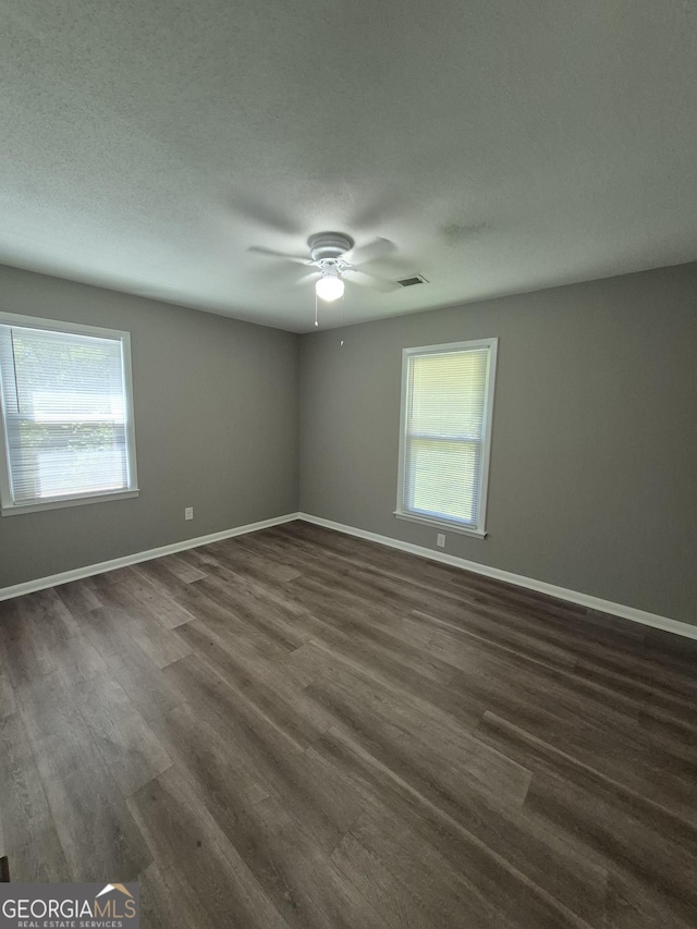 spare room with visible vents, ceiling fan, baseboards, and dark wood finished floors
