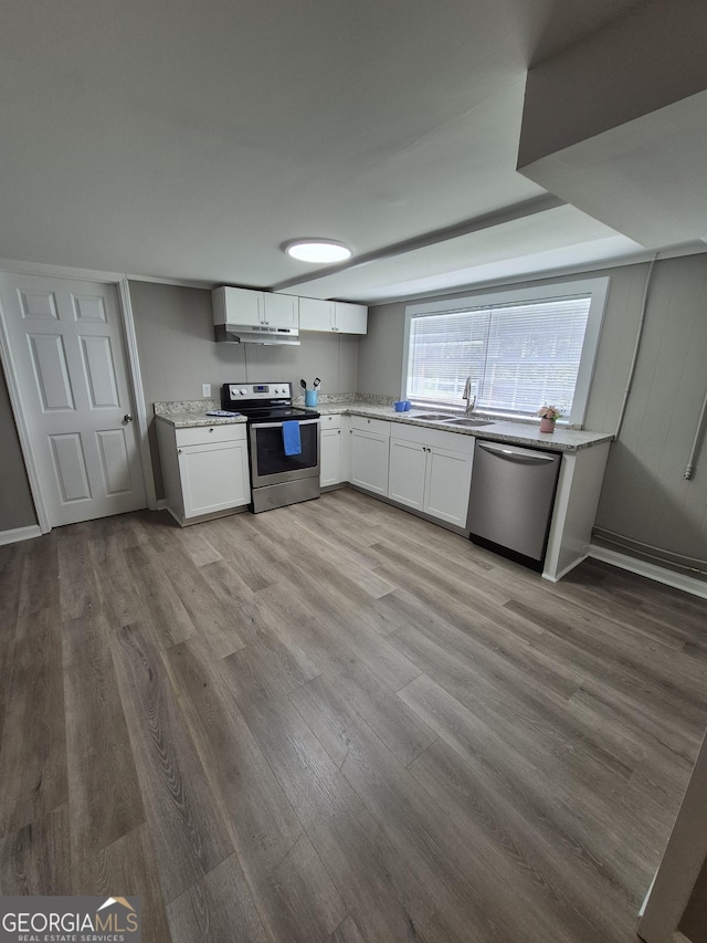 kitchen featuring light wood-type flooring, white cabinets, light stone countertops, stainless steel appliances, and a sink