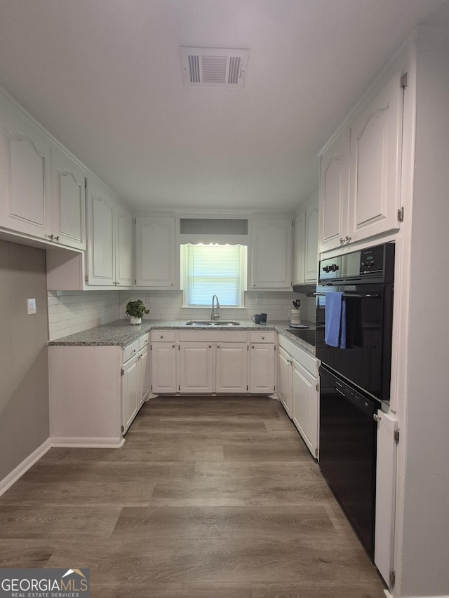 kitchen featuring visible vents, a sink, black appliances, white cabinetry, and decorative backsplash