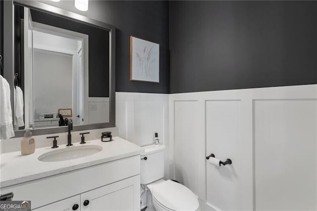 825 Maplewood Dr, Roswell, GA 30075 - half bathroom featuring a decorative wall, toilet, vanity, and wainscoting