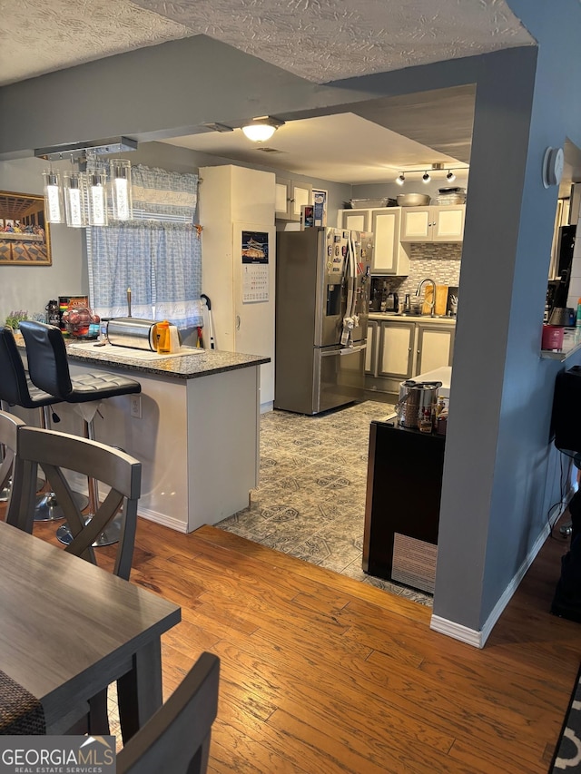 kitchen with stainless steel fridge with ice dispenser, light wood-style flooring, a textured ceiling, a sink, and decorative backsplash