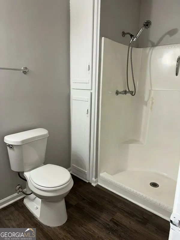 bathroom with a shower stall, wood finished floors, baseboards, and toilet