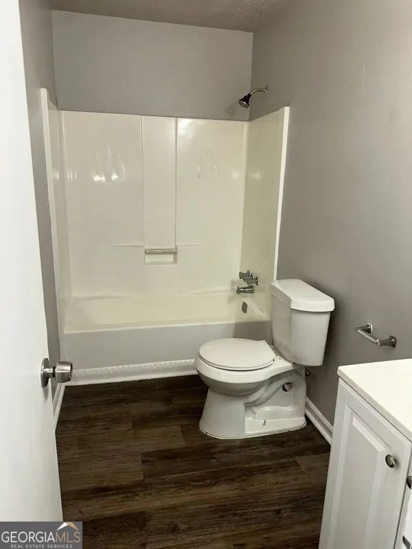 bathroom with washtub / shower combination, baseboards, toilet, vanity, and wood finished floors