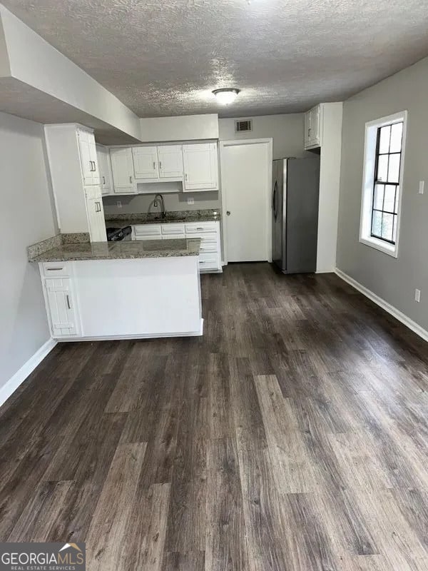 kitchen featuring a peninsula, freestanding refrigerator, dark wood-style floors, and visible vents