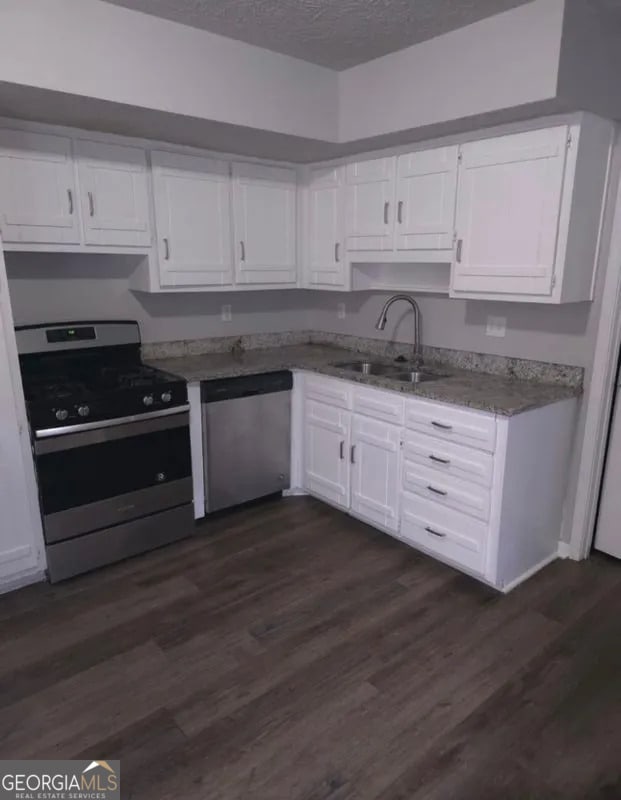 kitchen featuring dark wood-type flooring, a textured ceiling, white cabinets, a sink, and stainless steel appliances