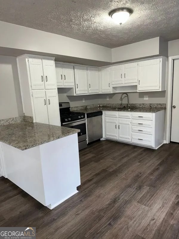 kitchen with dark stone countertops, appliances with stainless steel finishes, a peninsula, dark wood finished floors, and white cabinetry