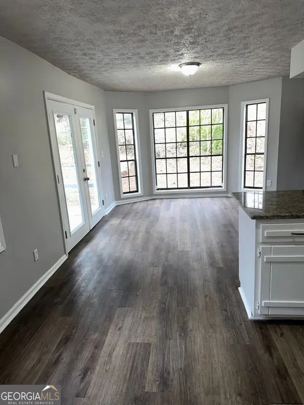 unfurnished dining area with dark wood-style flooring, baseboards, and a textured ceiling