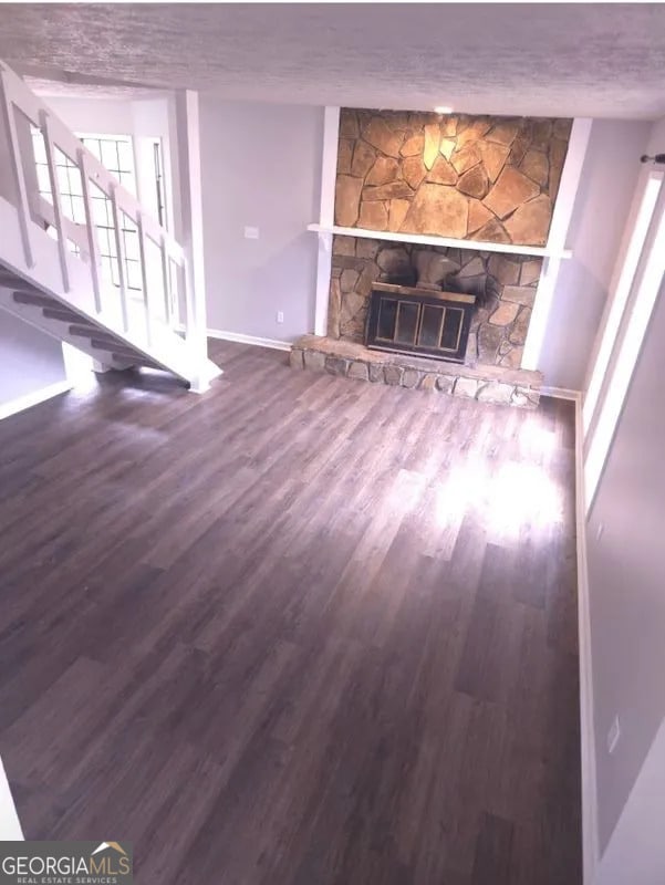 unfurnished living room featuring baseboards, a stone fireplace, a textured ceiling, wood finished floors, and stairs