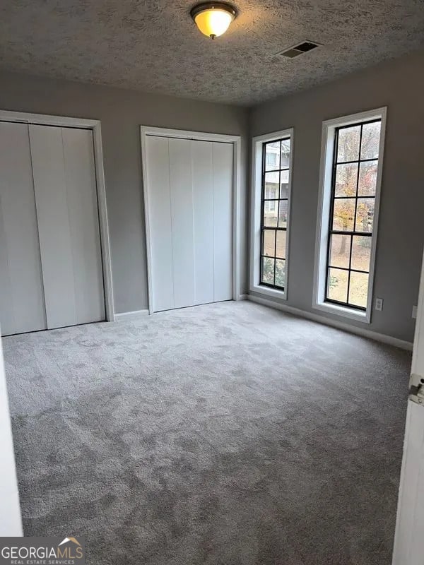 unfurnished bedroom featuring a textured ceiling, carpet, visible vents, and multiple closets