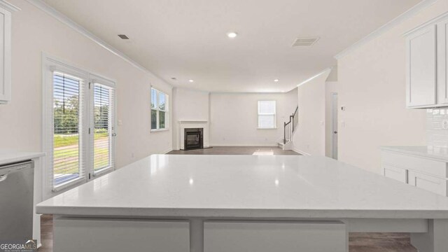 1139 Blue Juniper Cir, Loganville, GA 30052 - kitchen featuring stainless steel dishwasher, a glass covered fireplace, ornamental molding, white cabinets, and a kitchen island