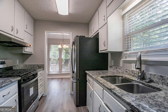 kitchen featuring an inviting chandelier, white cabinetry, under cabinet range hood, stainless steel range with gas stovetop, and a sink