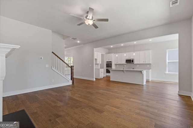 unfurnished living room with dark wood-type flooring, a ceiling fan, and visible vents