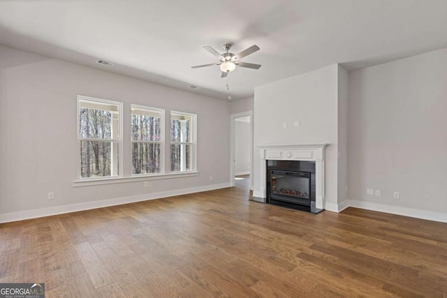 unfurnished living room featuring ceiling fan, a glass covered fireplace, wood finished floors, and baseboards
