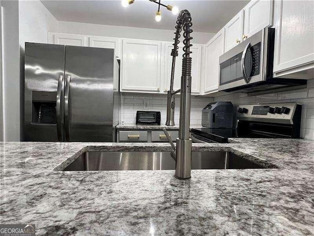 kitchen featuring white cabinetry, appliances with stainless steel finishes, light stone counters, and backsplash